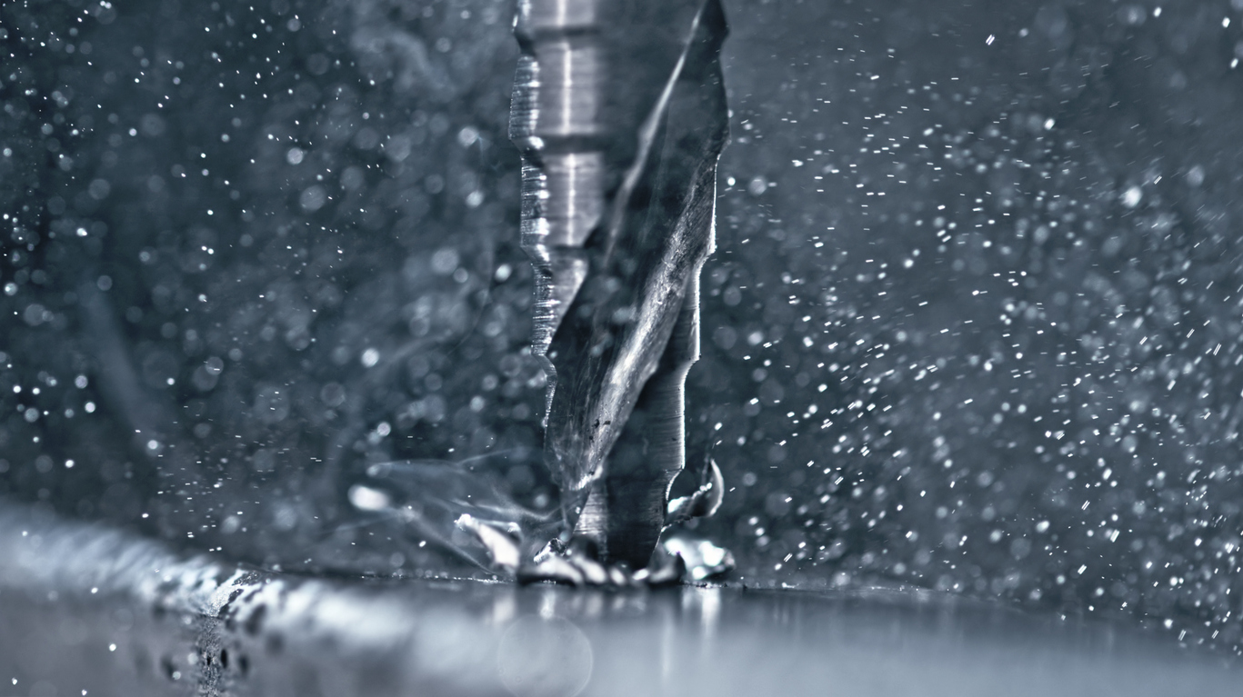 Macro photograph showcasing metallic drill bit penetrating aluminum surface, surrounded by scattered metal shavings and cooling liquid droplets in industrial manufacturing process.